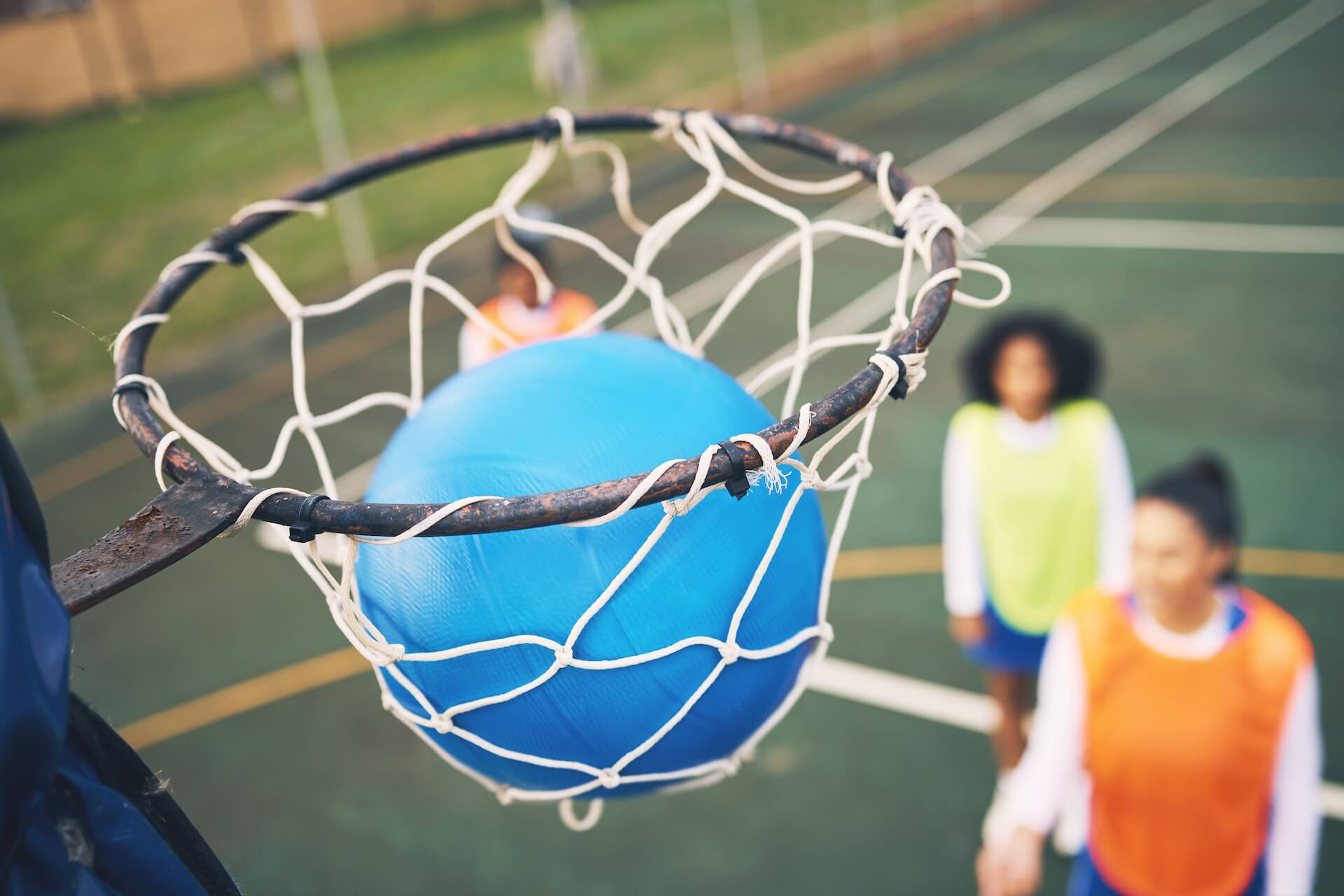 Netball going through a netball hoop | Featured image for the Netball Court Cleaning page from MKL Pressure Cleaning.